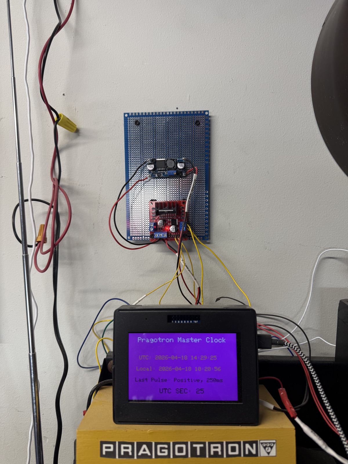Perfboard-mounted power stage showing a DC-DC buck converter and an L298N H-bridge motor driver module, with the master clock display visible below.