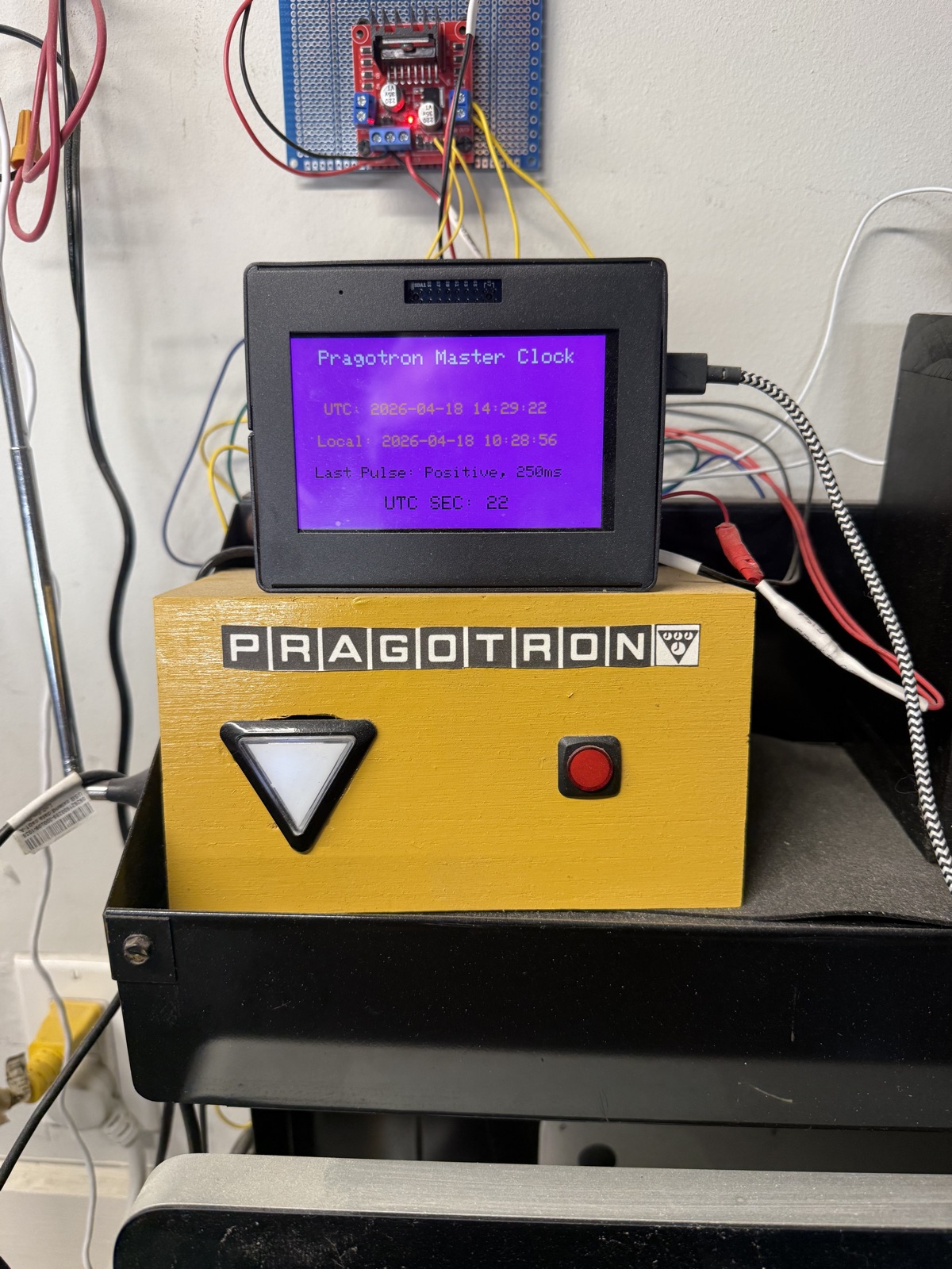 The finished master clock: a wooden enclosure with the Pragotron logo, a TFT display on top showing UTC and local time, last pulse information, and a UTC seconds counter.